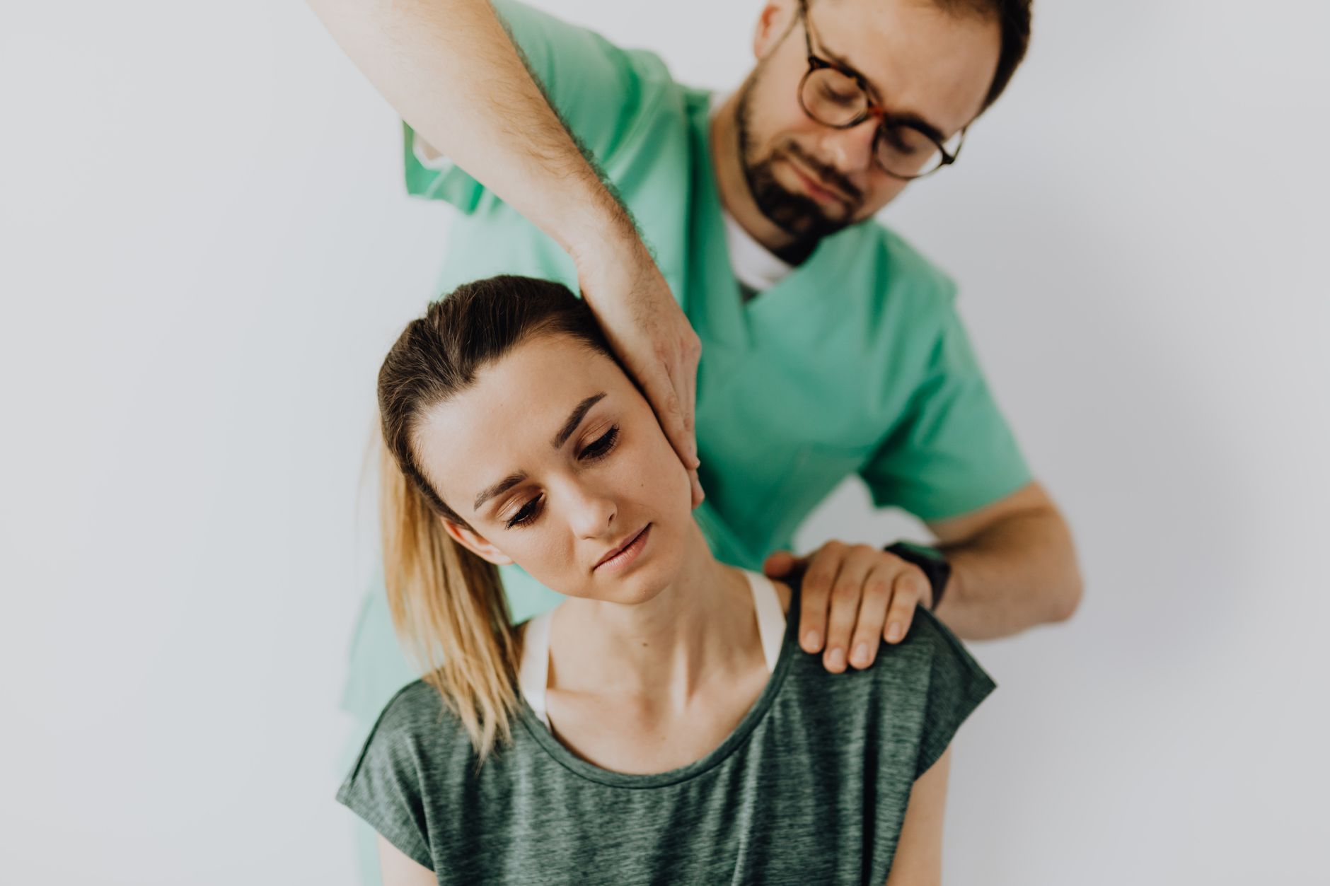 Therapist performs therapeutic neck massage on a calm young female patient in a medical setting.