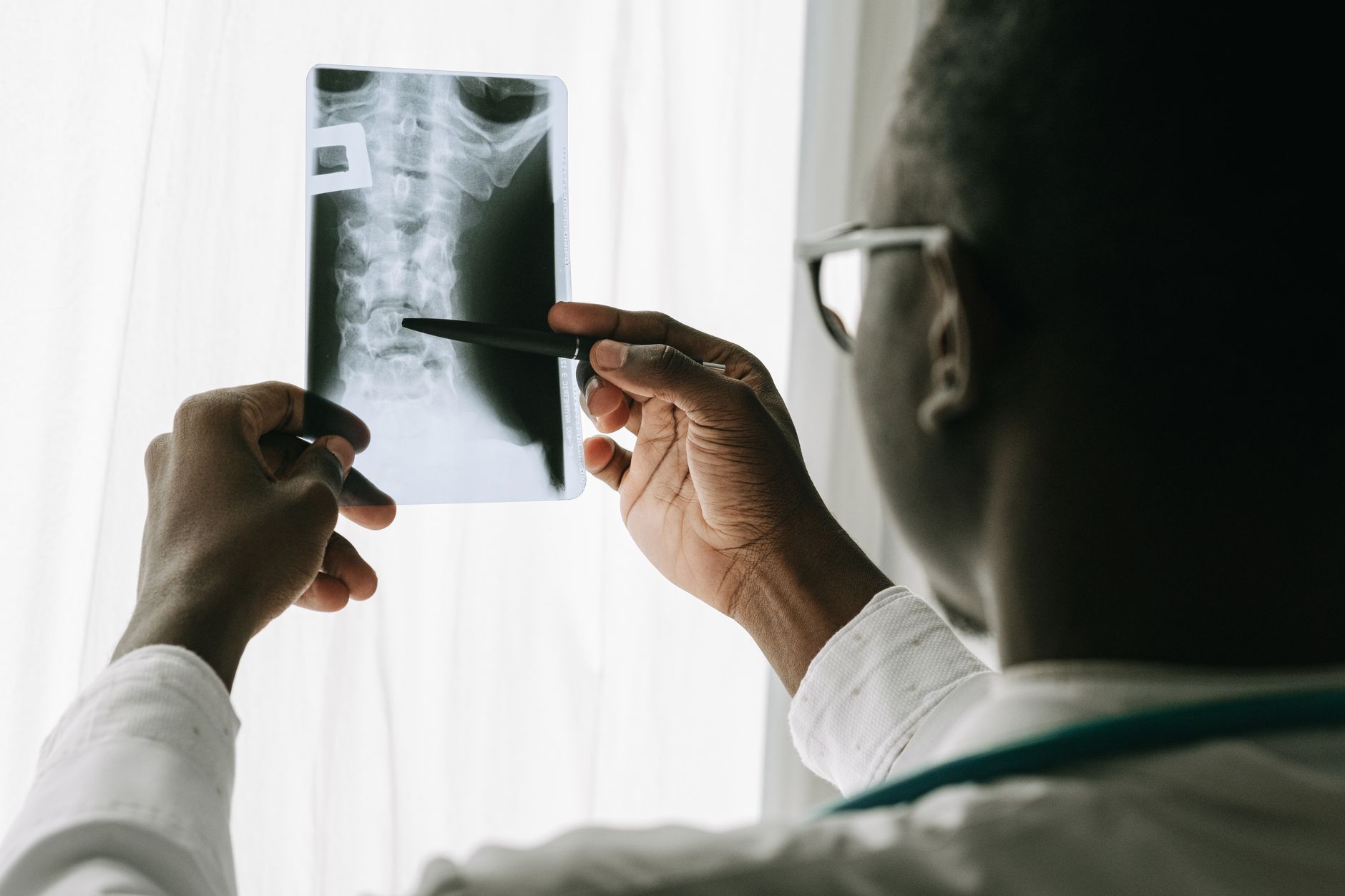 Doctor examining a spine X-ray film with a pen in a hospital setting.